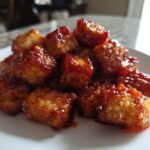 A pile of golden, crispy tofu cubes coated in a thick, shiny sweet chili glaze.