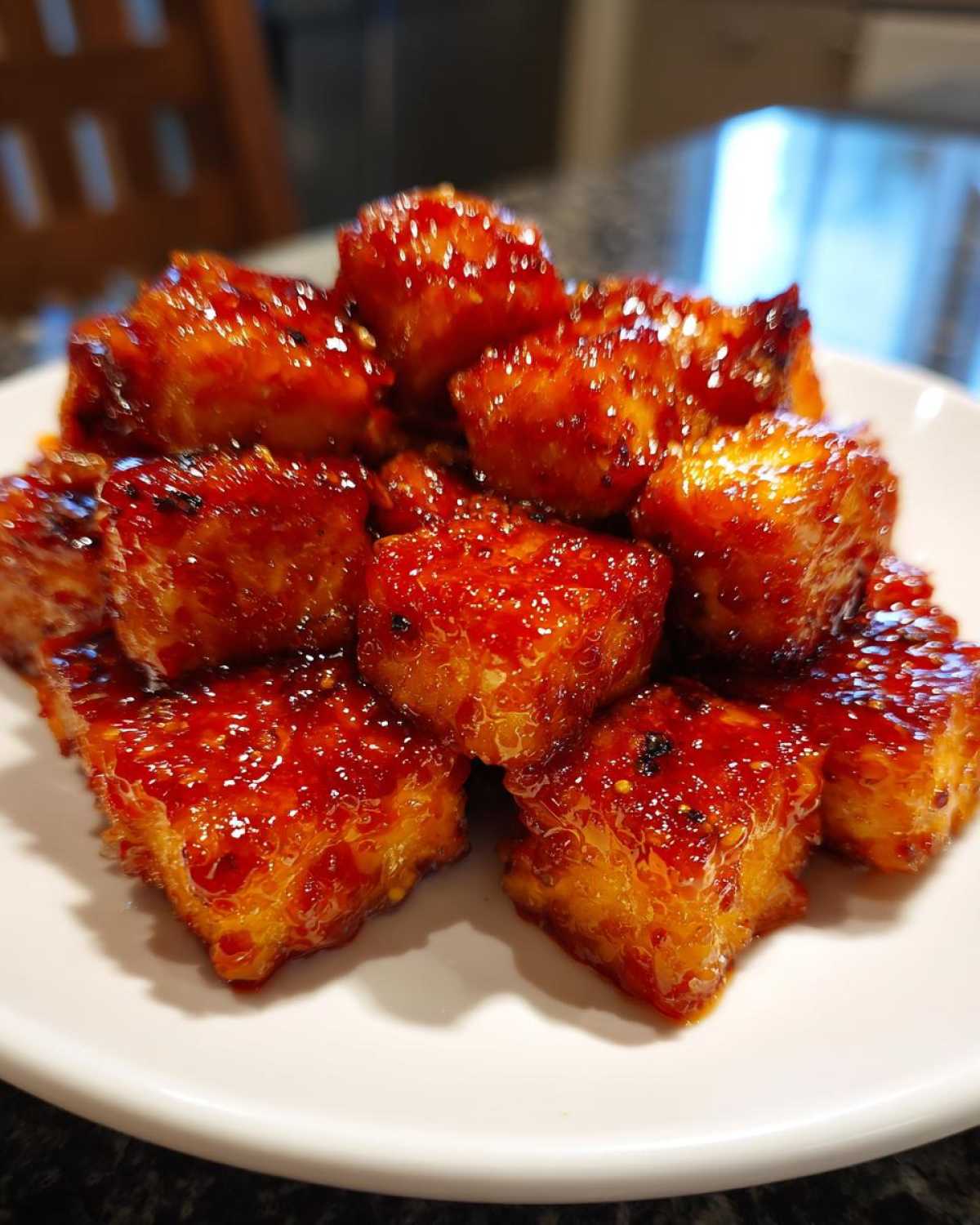 Close-up of crispy, glazed tofu cubes coated in a sticky, bright red sweet chili glaze.