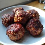A close-up of six perfectly browned Air Fryer Italian Meatballs resting on a white plate.