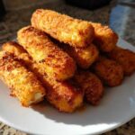 A pile of crispy, golden brown Air Fryer Mozzarella Sticks stacked high on a white plate.
