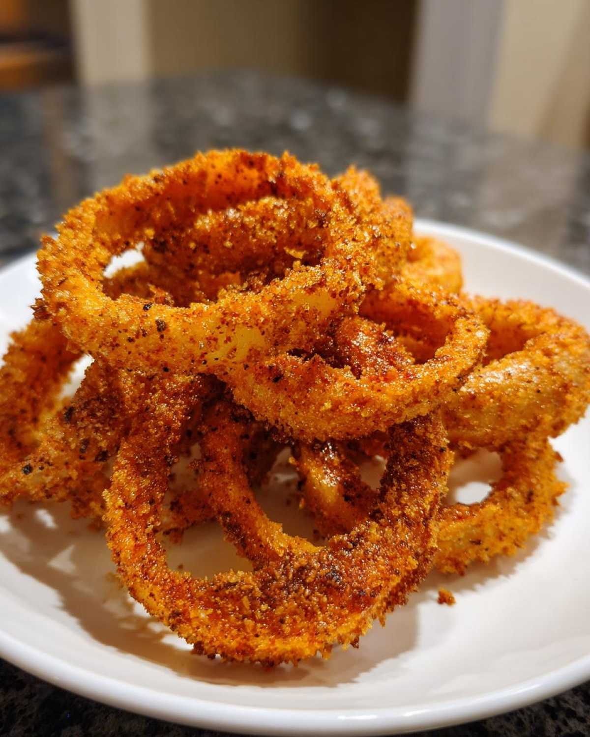 A close-up of a pile of golden brown, crispy Air Fryer Onion Rings seasoned with spices on a white plate.