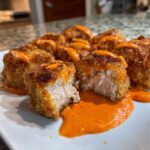 Close-up of crispy Air Fryer Salmon Bites drizzled with bright orange Bang Bang Sauce, one piece cut open showing flaky salmon inside.