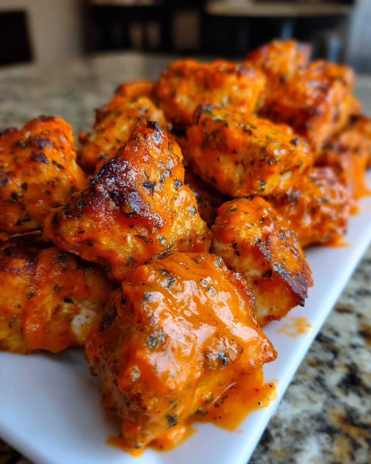 Close-up of crispy, saucy Air Fryer Salmon Bites coated in bright orange Bang Bang Sauce, served on a white platter.