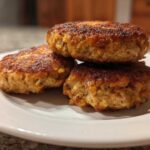 Three perfectly cooked Air Fryer Salmon Patties stacked on a white plate, showing a golden-brown, crispy exterior.