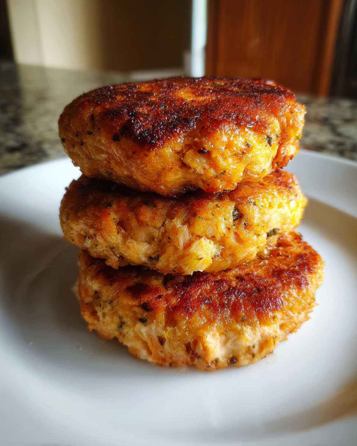 A stack of three perfectly cooked Air Fryer Salmon Patties with a golden-brown, crispy exterior on a white plate.
