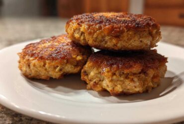 Three perfectly cooked Air Fryer Salmon Patties stacked on a white plate, showing a golden-brown, crispy exterior.