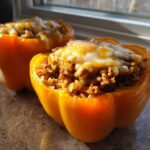 Two bright yellow Air Fryer Stuffed Bell Peppers filled with seasoned rice and meat, topped with melted cheese.