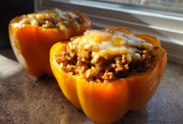 Two bright yellow Air Fryer Stuffed Bell Peppers filled with seasoned rice and meat, topped with melted cheese.