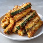 A stack of golden brown Air Fryer Zucchini Fries with Parmesan piled high on a white plate.