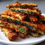 A close-up stack of crispy, golden-brown Air Fryer Zucchini Fries with Parmesan piled high on a white plate.