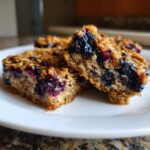 Two rich, moist Blueberry Baked Oatmeal Squares showing the texture of oats and burst blueberries.