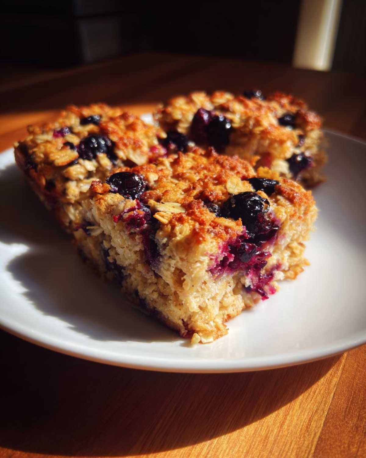 Three squares of golden-brown Blueberry Baked Oatmeal Squares studded with dark blueberries on a white plate.