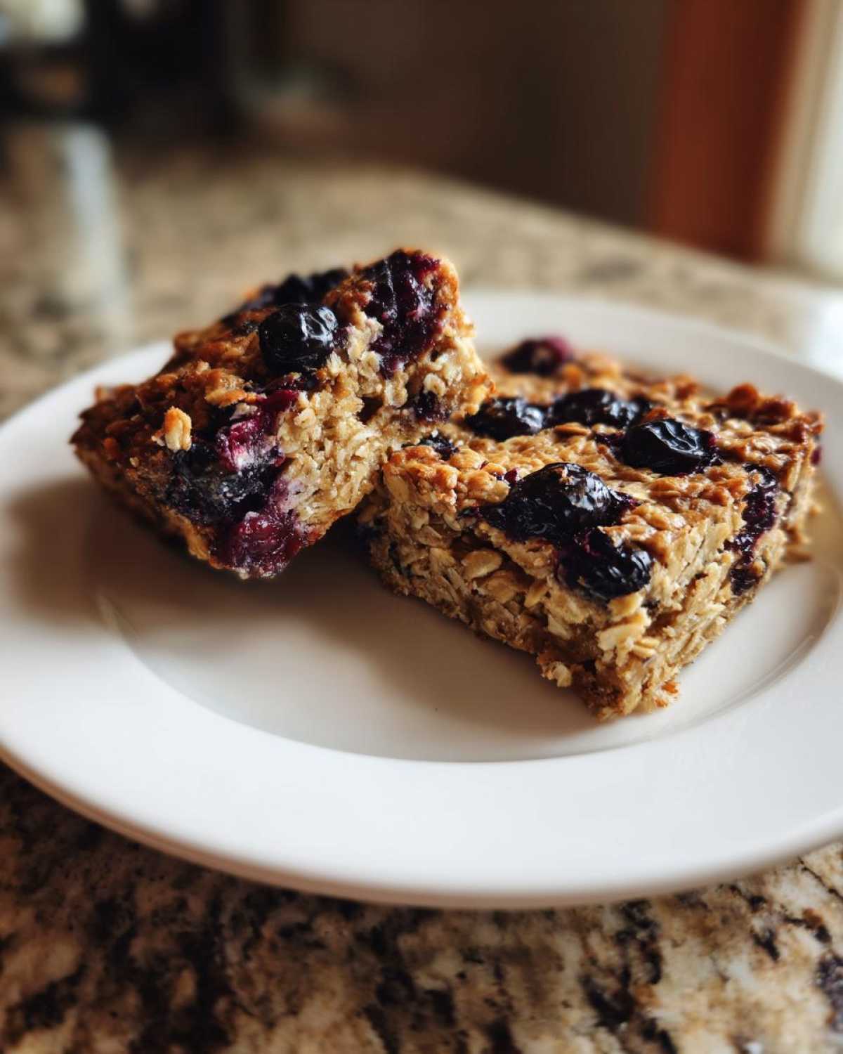 Two moist Blueberry Baked Oatmeal Squares, studded with dark blueberries, resting on a white plate.