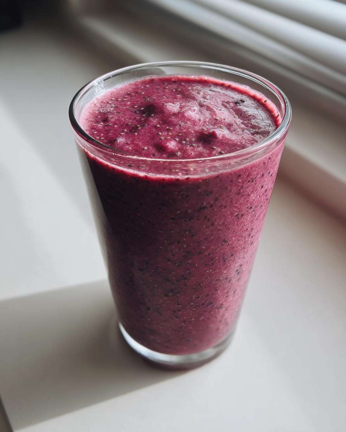 A tall glass filled with a thick, deep purple Blueberry Lemon Chia Smoothie showing visible chia seeds.