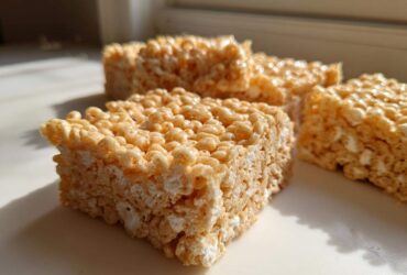 Close-up of several squares of chewy Brown Butter Rice Krispie Treat Bars sitting on a white surface near a window.