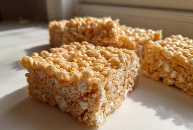 Close-up of several squares of chewy Brown Butter Rice Krispie Treat Bars sitting on a white surface near a window.