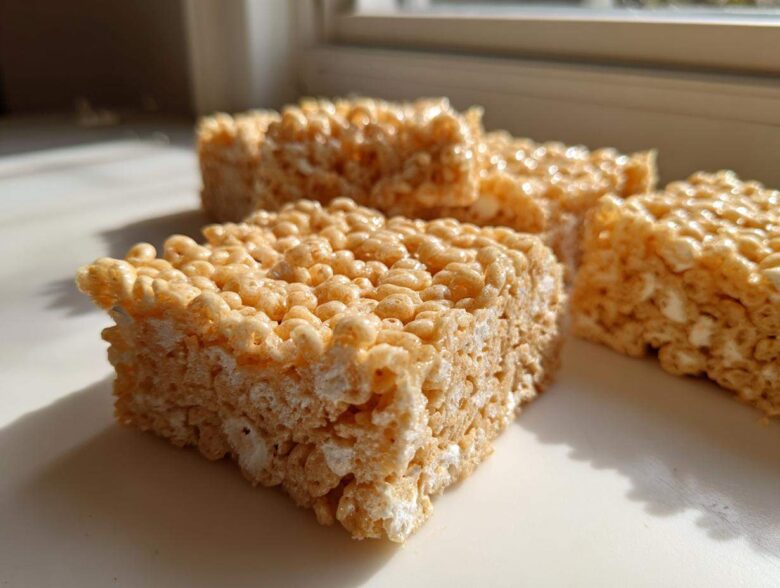 Close-up of several squares of chewy Brown Butter Rice Krispie Treat Bars sitting on a white surface near a window.