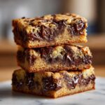 Three thick, chewy chocolate chip cookie bars stacked, showing molten chocolate chips inside.