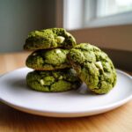 A stack of four vibrant green, chewy matcha white chocolate cookies with visible white chocolate chips.