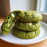 A stack of three vibrant green Chewy Matcha White Chocolate Cookies, with one cookie broken open revealing the soft interior and white chocolate chunks.