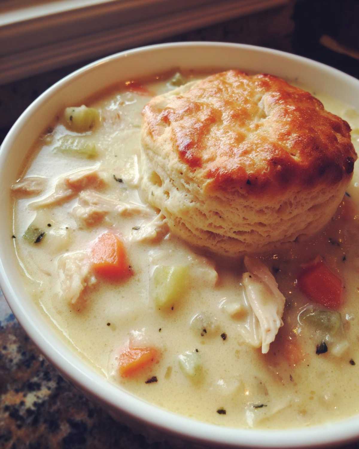 A close-up of creamy Chicken Pot Pie Soup filled with vegetables and topped with a golden biscuit.