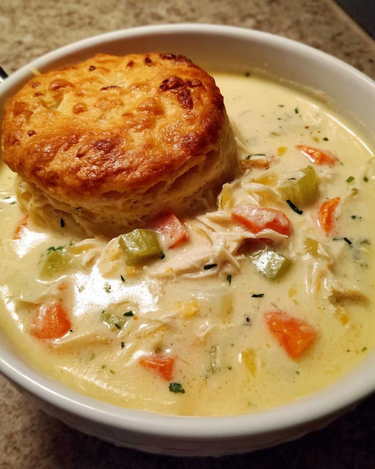A creamy bowl of Chicken Pot Pie Soup topped with a golden brown biscuit.
