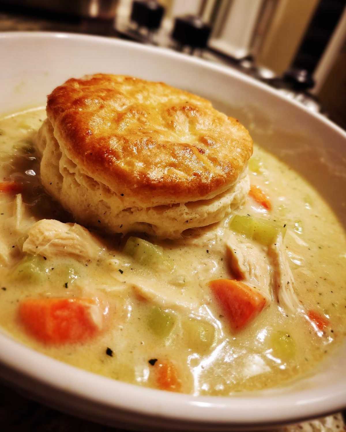 Close-up of creamy Chicken Pot Pie Soup topped with a golden brown biscuit.