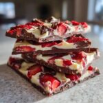 A stack of four rich pieces of Chocolate Covered Strawberry Bark featuring dark chocolate, white chocolate swirls, and fresh strawberry slices.