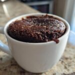 Close-up of a rich Chocolate Lava Mug Cake baked inside a white mug, with molten chocolate dripping over the edge.