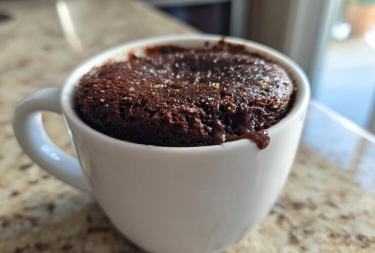 Close-up of a rich Chocolate Lava Mug Cake baked inside a white mug, with molten chocolate dripping over the edge.
