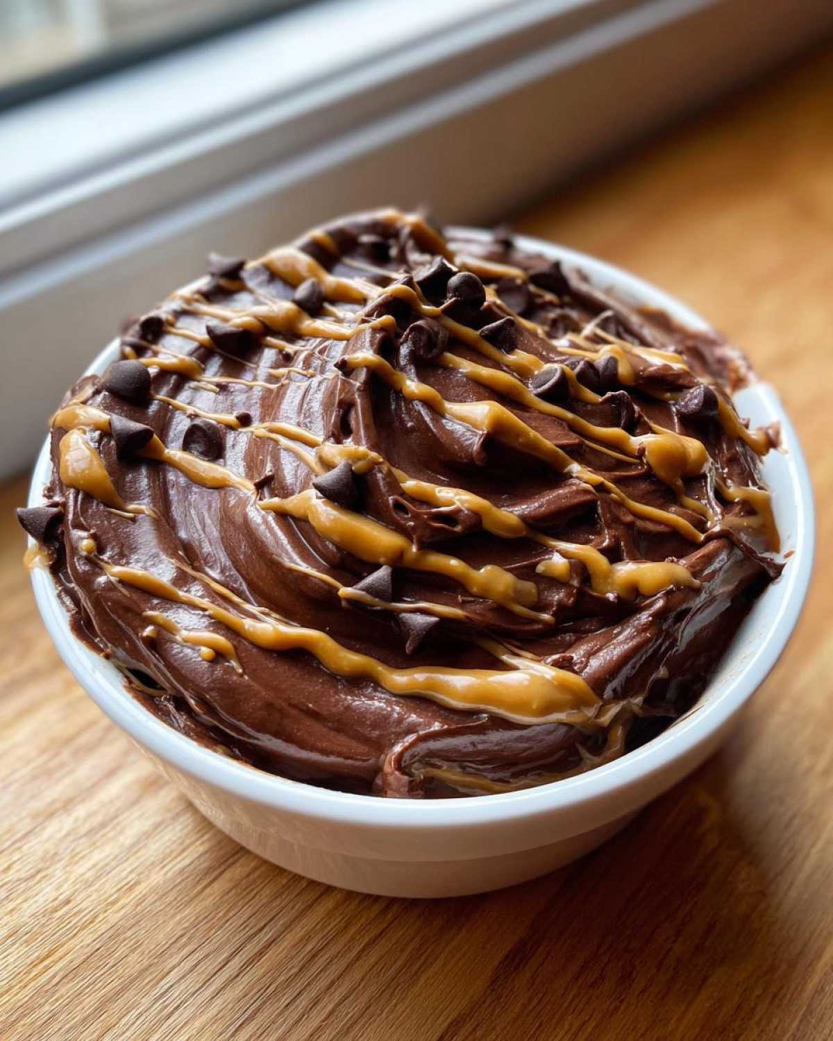 Close-up of rich Chocolate Peanut Butter Cheesecake Dip topped with peanut butter drizzle and mini chocolate chips.