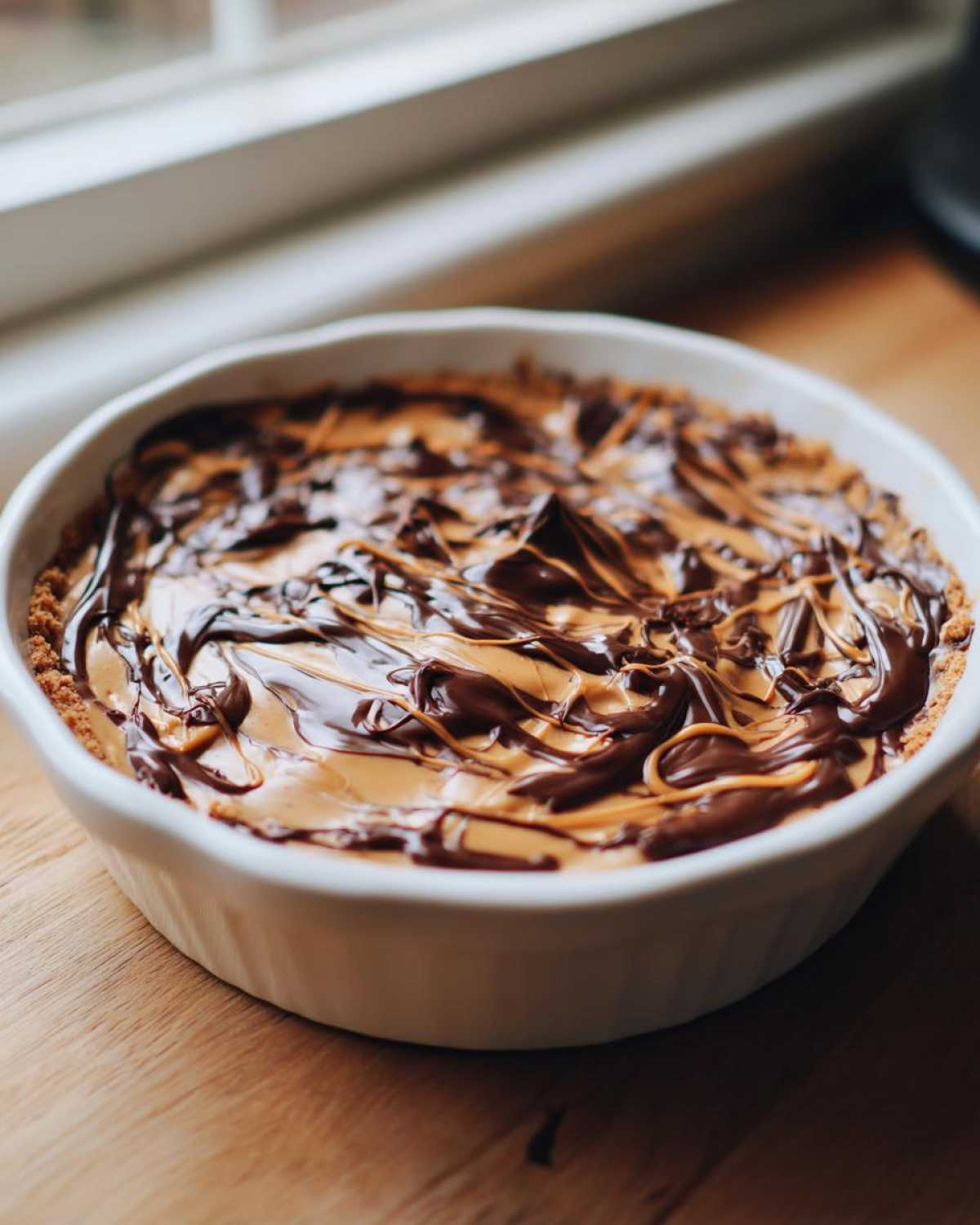A white dish filled with Chocolate Peanut Butter Cheesecake Dip, topped with swirled chocolate.