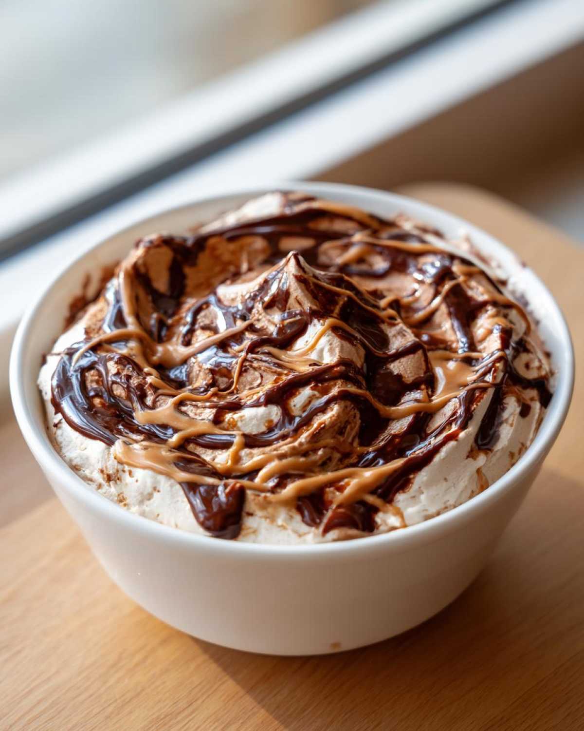 A white bowl filled with rich Chocolate Peanut Butter Cheesecake Dip, topped with swirls of chocolate syrup and peanut butter.