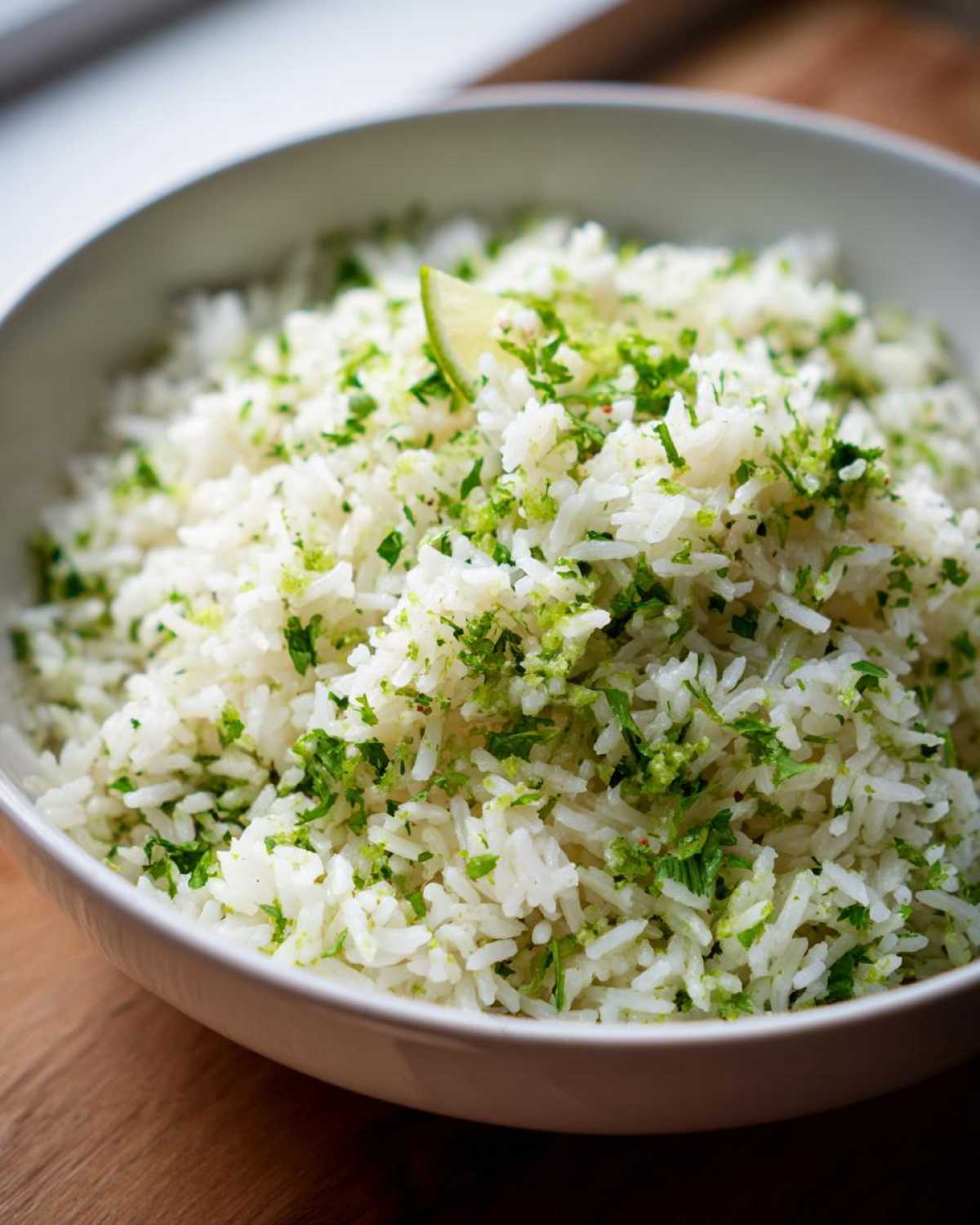 A close-up of fluffy white rice mixed with bright green cilantro and lime zest, served in a white bowl.
