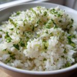 Close-up of fluffy white rice seasoned with bright green cilantro and lime zest, served in a white bowl.