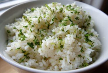 Close-up of fluffy white rice seasoned with bright green cilantro and lime zest, served in a white bowl.