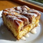 A close-up of a square slice of Cinnamon Roll Overnight French Toast Bake drizzled with white icing.