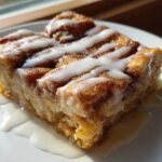 Close-up of a square serving of Cinnamon Roll Overnight French Toast Bake drizzled with white icing.