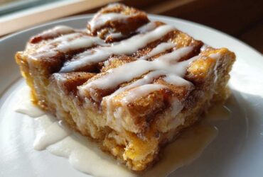 Close-up of a square serving of Cinnamon Roll Overnight French Toast Bake drizzled with white icing.
