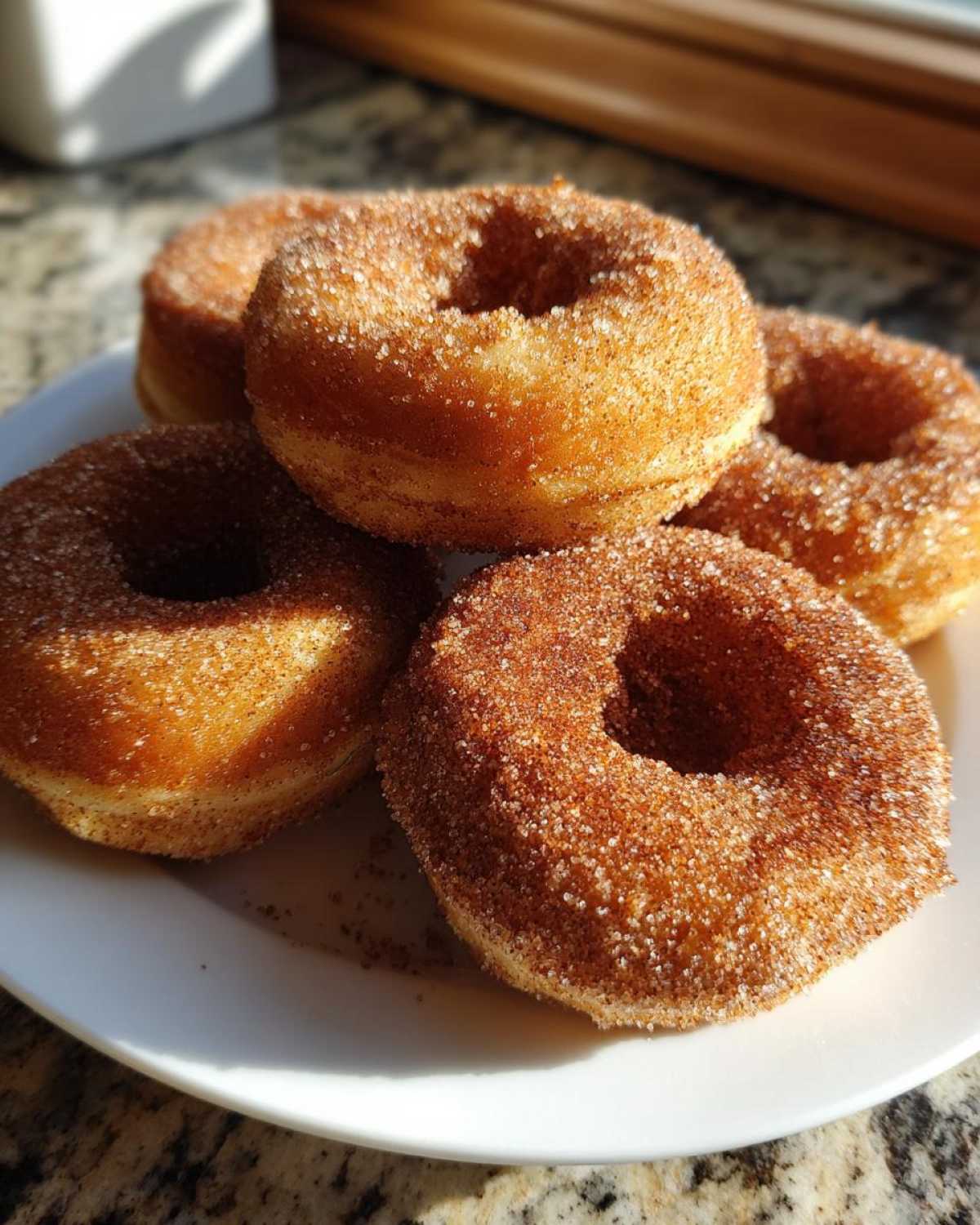 Four golden brown Cinnamon Sugar Air Fryer Donuts heavily coated in sparkling cinnamon sugar, stacked on a white plate.