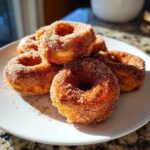 A stack of freshly made Cinnamon Sugar Air Fryer Donuts heavily coated in sparkling cinnamon sugar on a white plate.