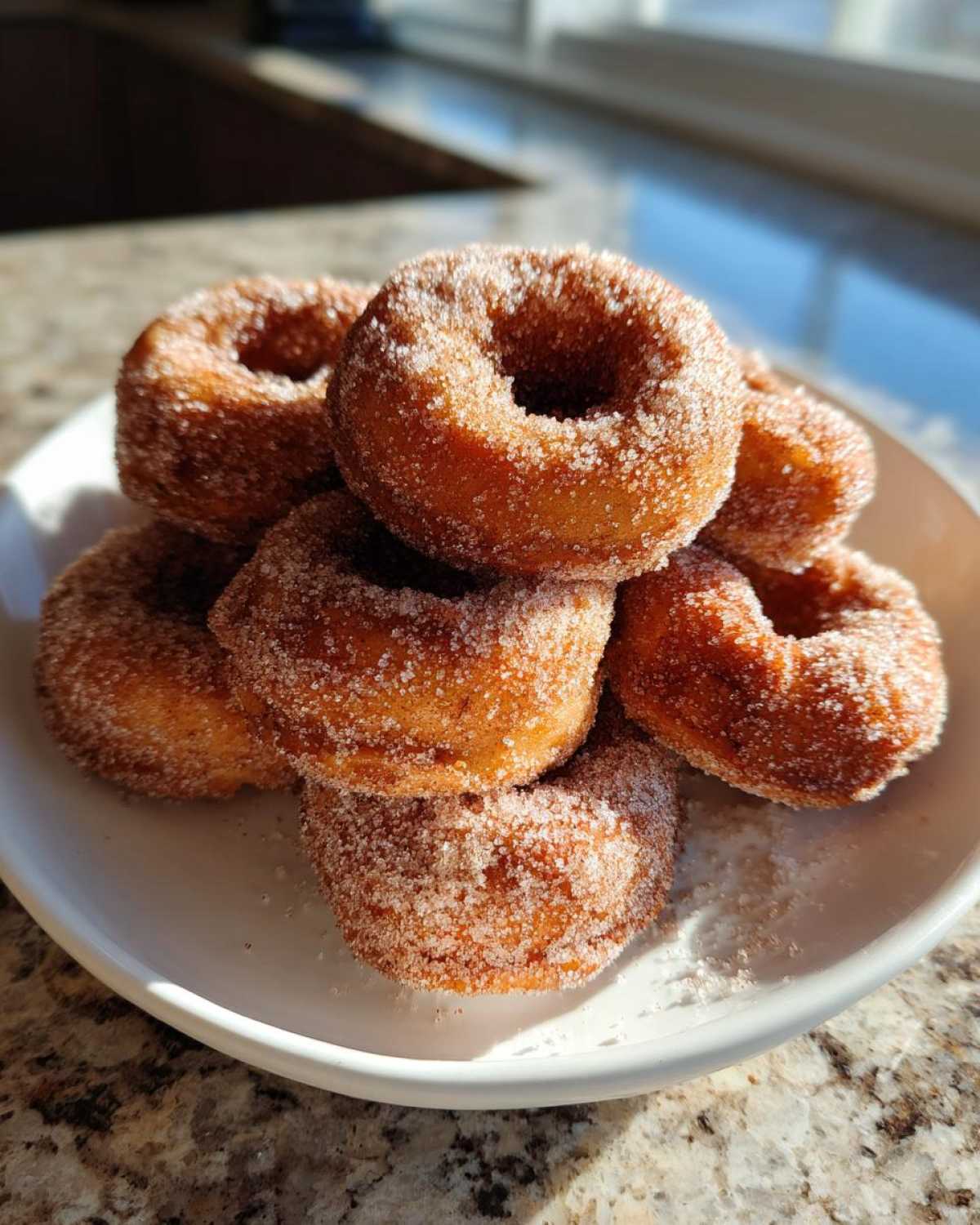 A stack of freshly made Cinnamon Sugar Air Fryer Donuts heavily coated in sparkling sugar, resting on a white plate.