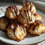 A stack of golden Coconut Macaroons with Dark Chocolate Drizzle on a light ceramic plate.