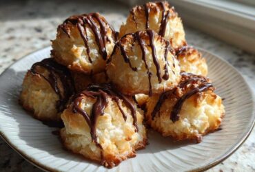 A stack of golden Coconut Macaroons with Dark Chocolate Drizzle on a light ceramic plate.