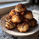 A stack of golden Coconut Macaroons with Dark Chocolate Drizzle on a light gray plate.
