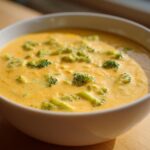A creamy, orange-yellow bowl of Copycat Broccoli Cheddar Soup featuring visible green florets.
