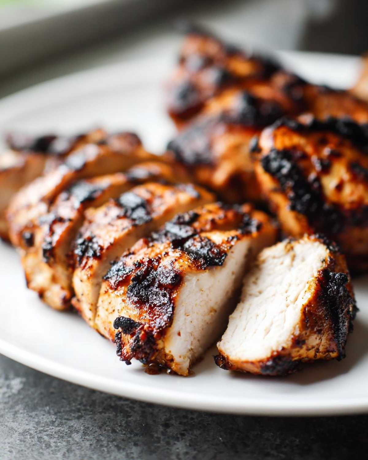 Close-up of sliced, grilled Copycat Chipotle Chicken showing juicy white meat and charred edges on a white plate.