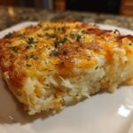 A close-up serving of golden brown Copycat Cracker Barrel Hashbrown Casserole topped with melted cheese and parsley.