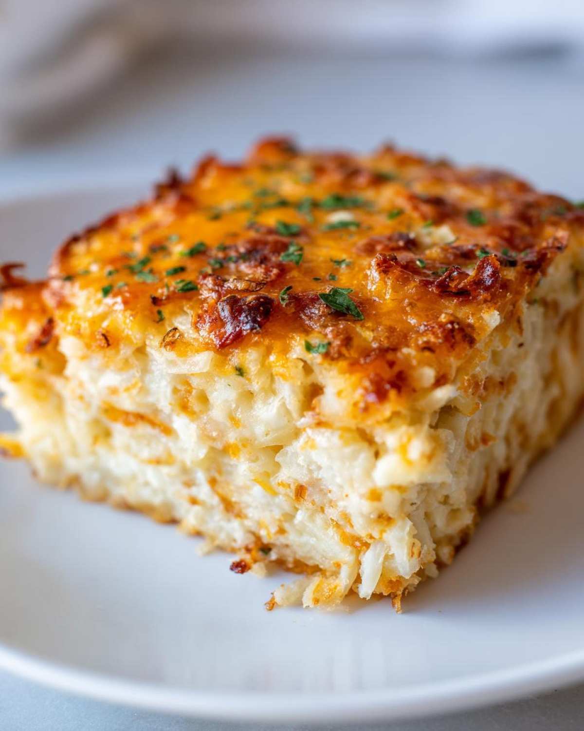 A close-up of a square serving of Copycat Cracker Barrel Hashbrown Casserole with a golden, cheesy crust.