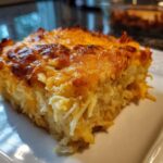 Close-up of a cheesy, baked slice of Copycat Cracker Barrel Hashbrown Casserole on a white plate.